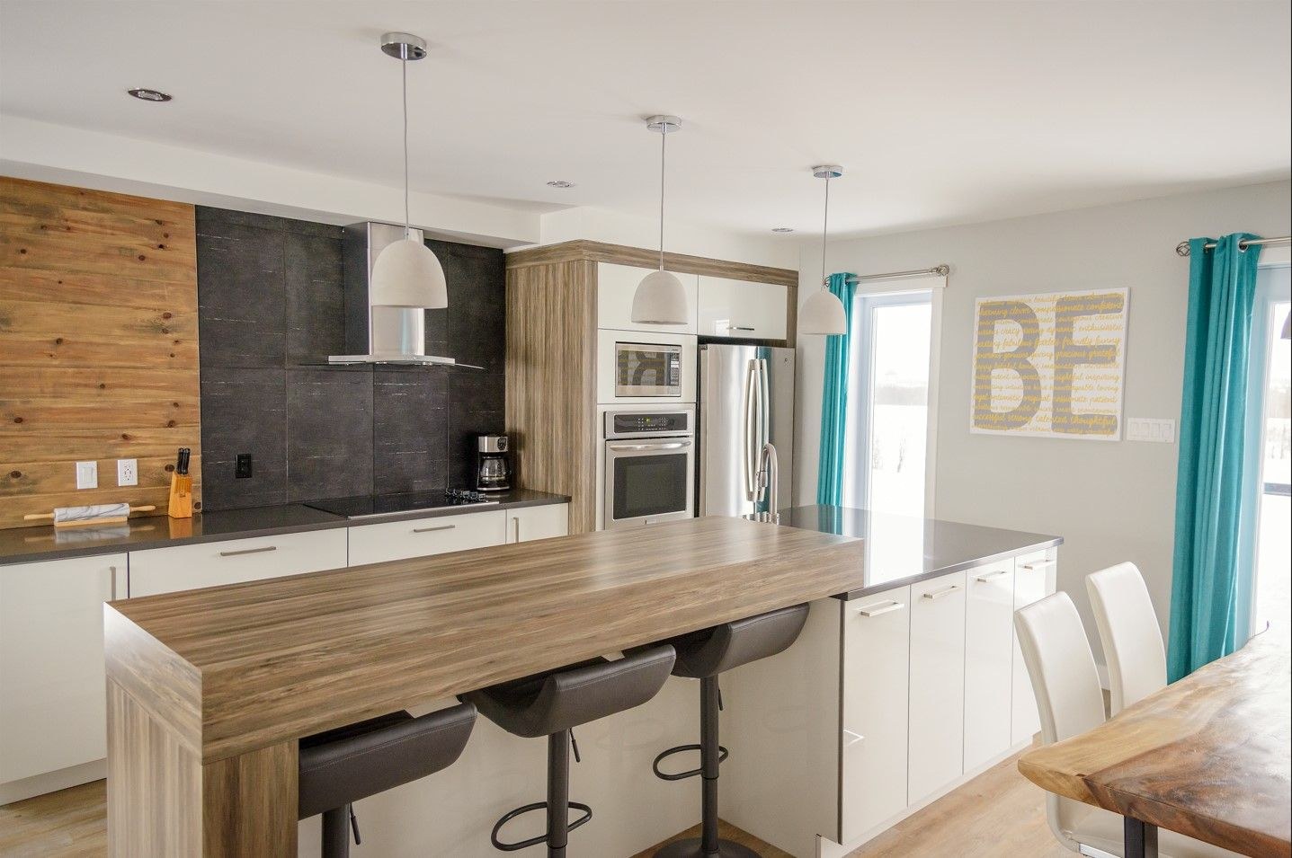 Mur d'accent en lattes de bois, îlot blanc avec comptoir de bois, four encastré et rideaux turquoise.